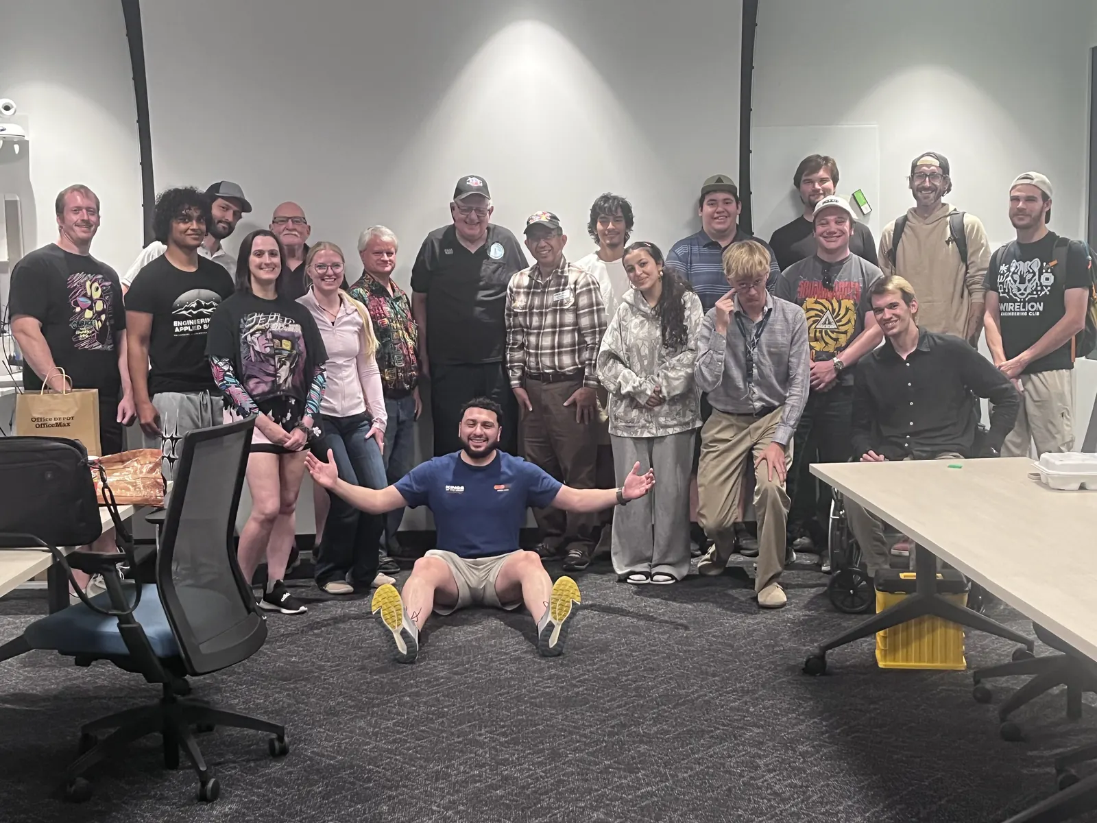 Group photo of Wire Lion members at a club meeting, with one member sitting on the floor in front, arms spread wide
