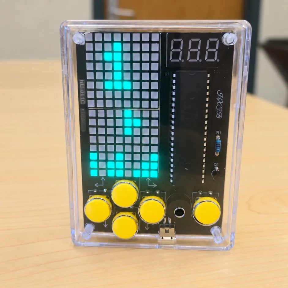 Completed HU-001C handheld game machine in a clear case with yellow buttons and a lit green LED matrix